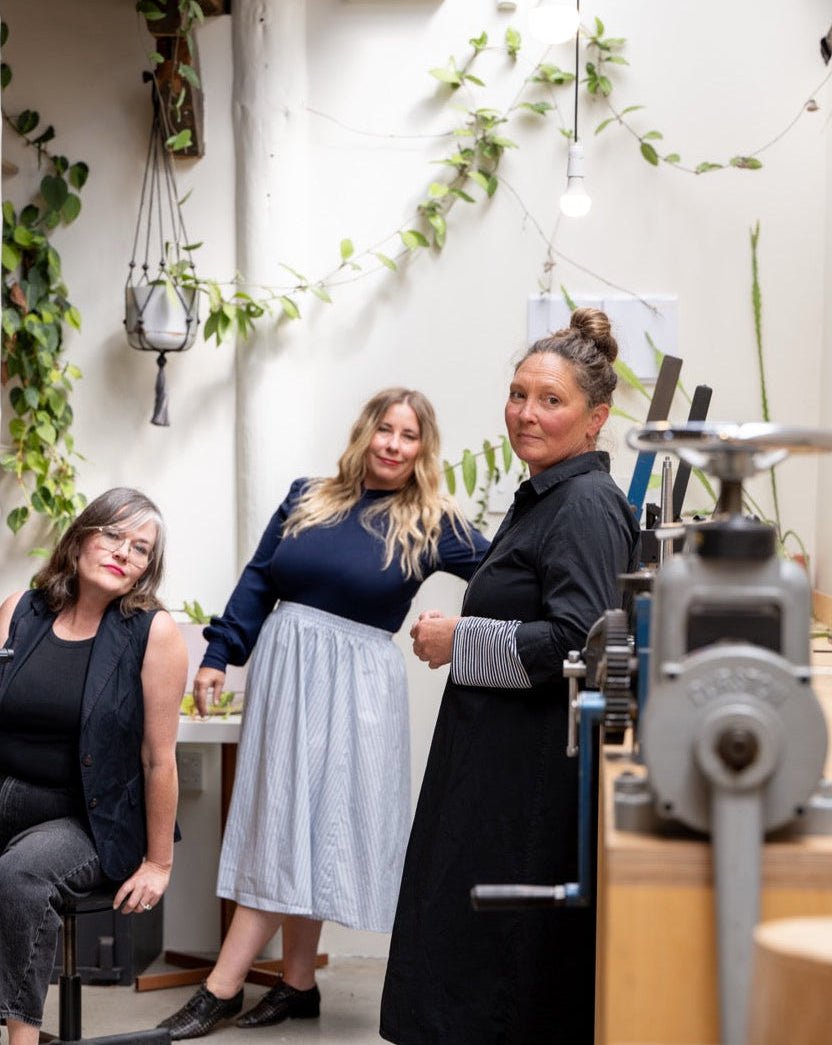 Three women standing in a room with plants and office equipment.
